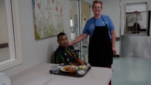 A member of kitchen staff and a resident smile at a skilled nursing facility